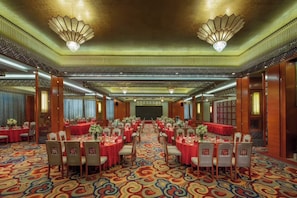 Un salón de banquetes con mesas redondas, sillas y una alfombra estampada.