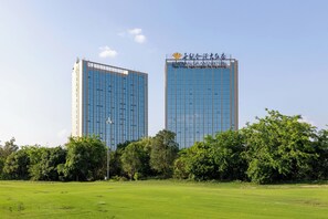 Dos edificios altos con fachadas de vidrio reflectante, rodeados por un campo cubierto de césped y árboles frondosos.