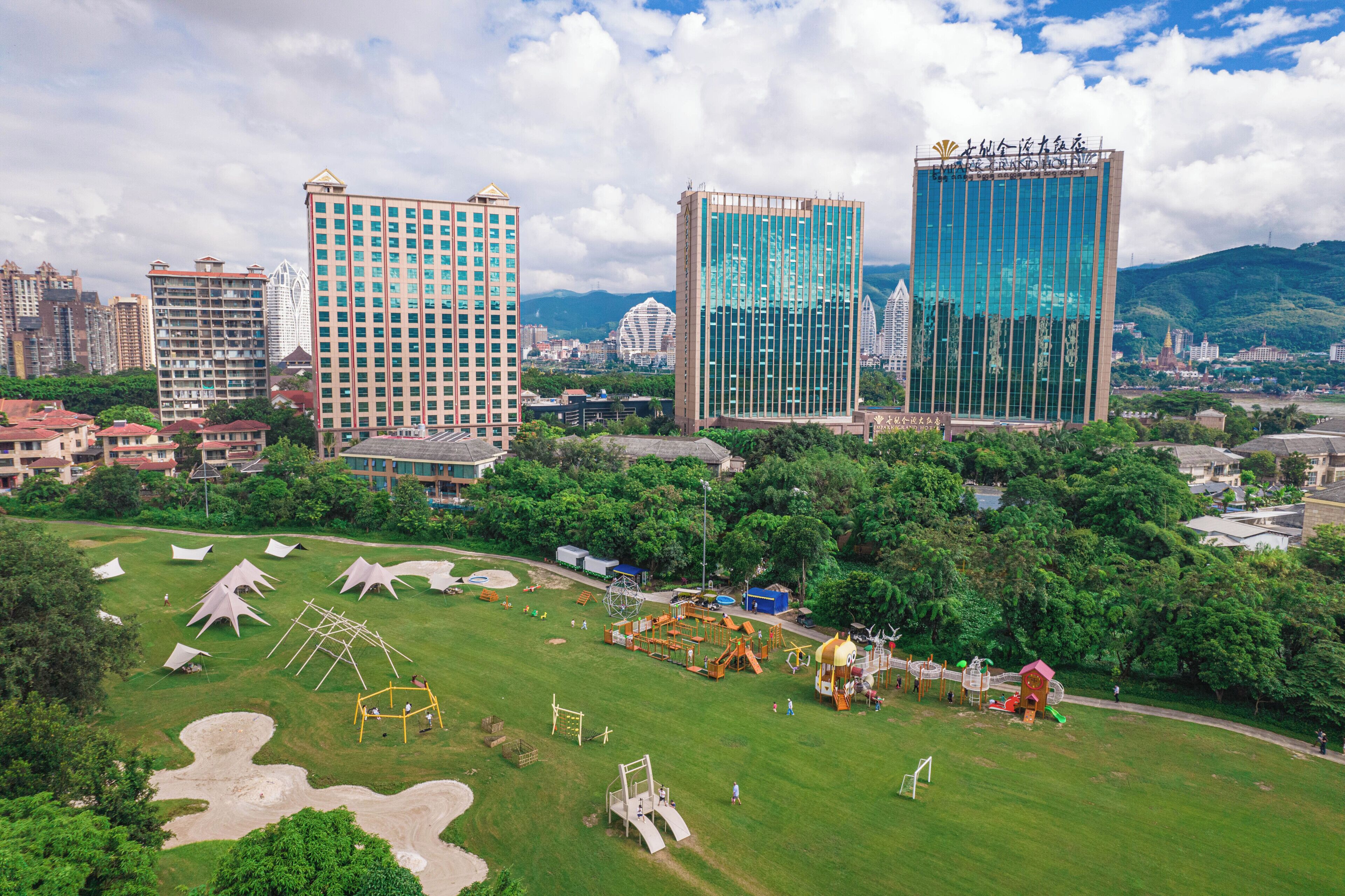 A cityscape with modern high-rise buildings, a park with playgrounds, and a clear sky.