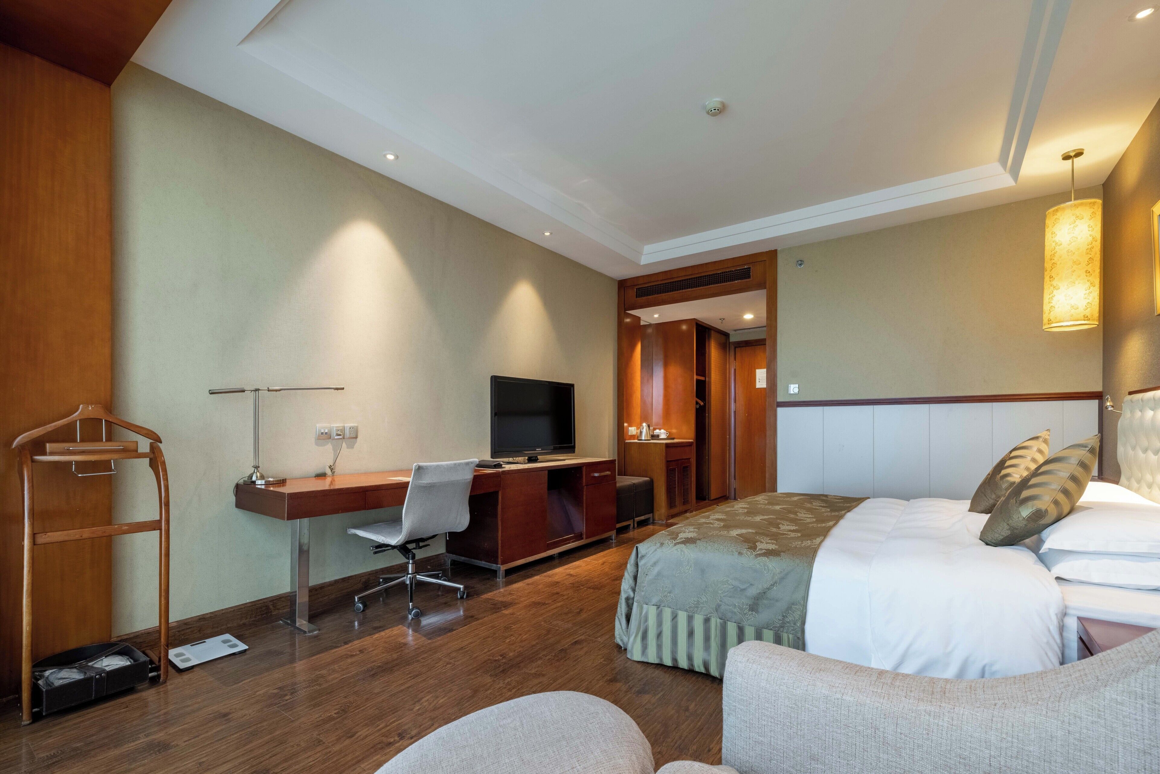 A hotel room with a bed, a desk with a chair, a television, and a wardrobe.