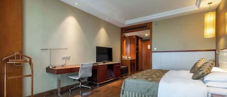 Una habitación de hotel con cama, escritorio con silla, televisor y armario.