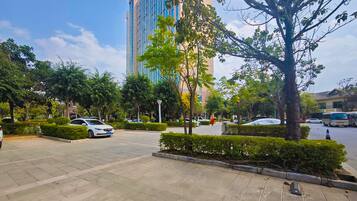 A paved outdoor area with a car, trees, and a tall building in the background.