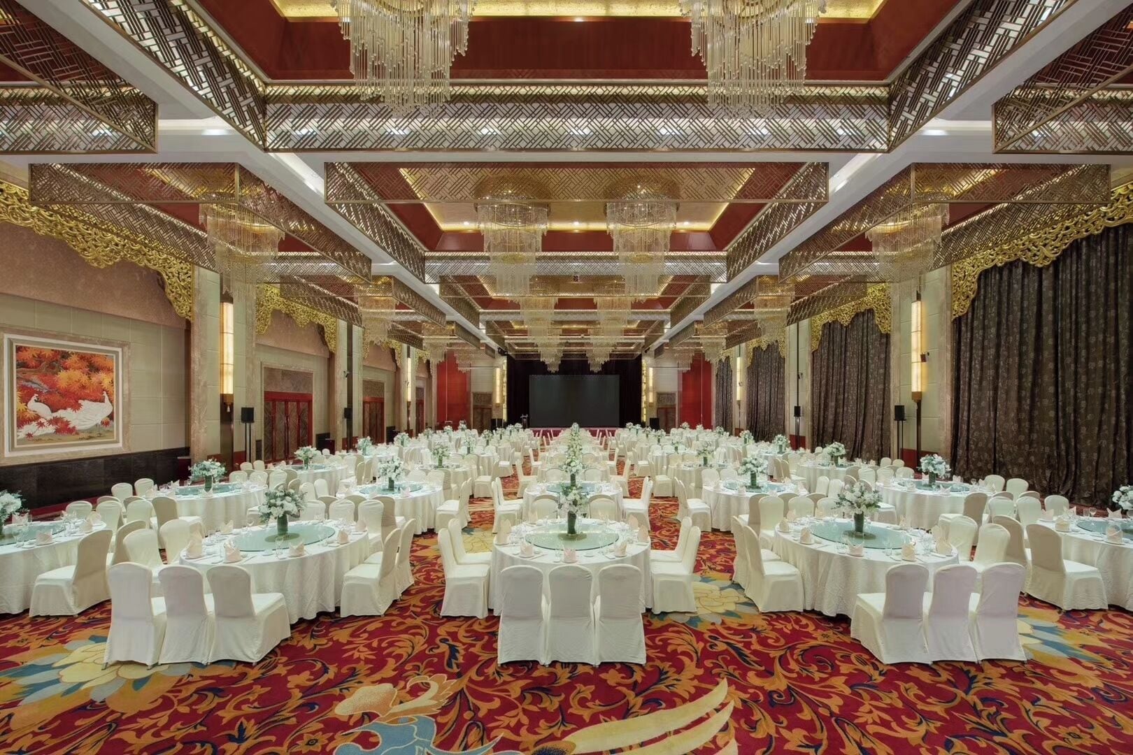 A banquet hall with round tables, white chairs, and a red carpet.
