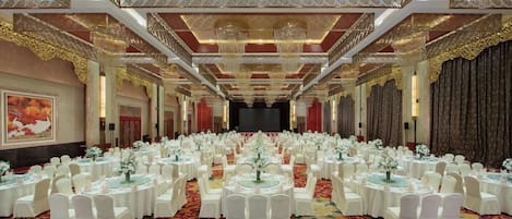 A banquet hall with round tables, white chairs, and a red carpet.