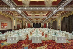 Un salón de banquetes con mesas redondas, sillas blancas y una alfombra roja.