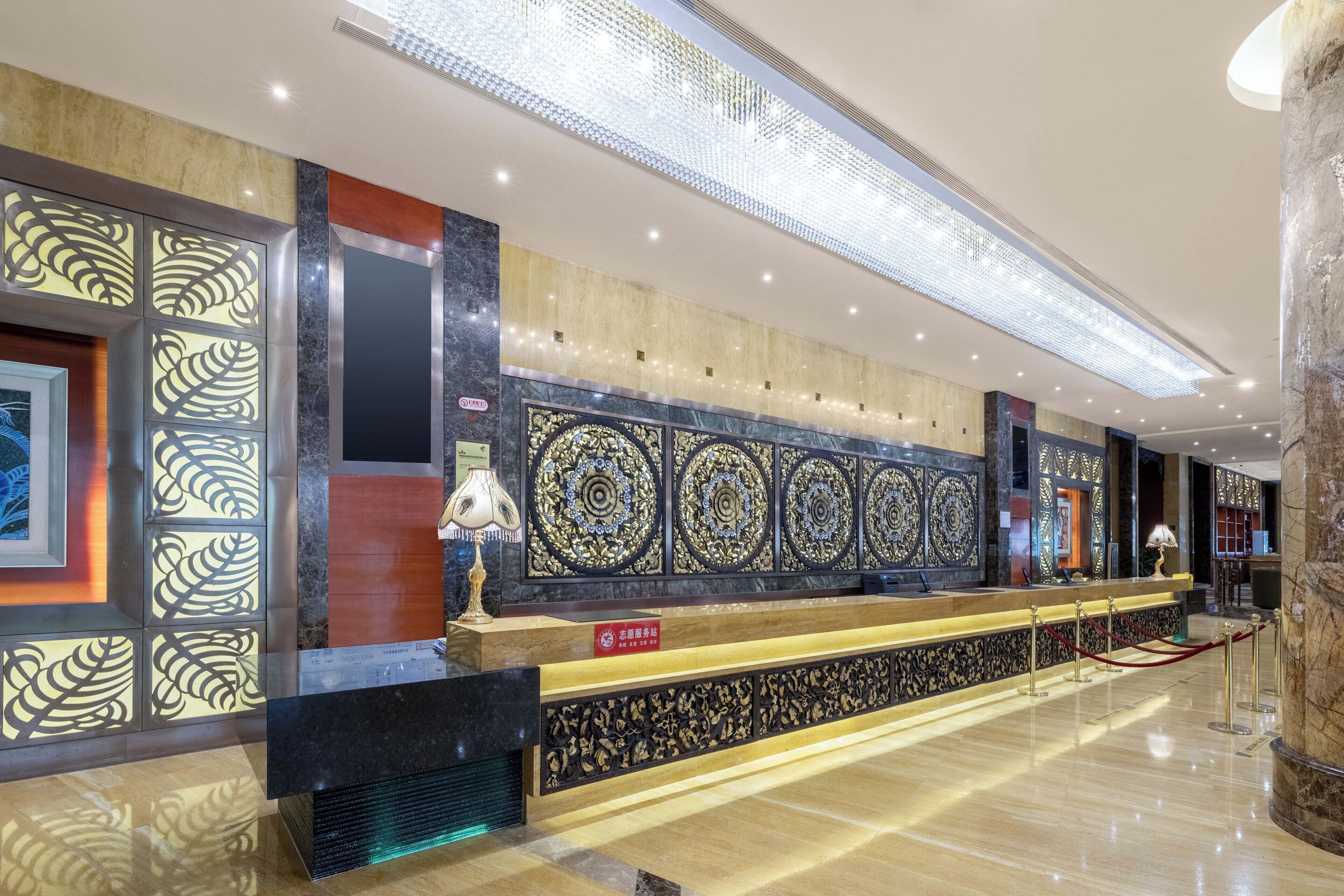 Een hotel receptie met een marmeren balie, decoratieve wandpanelen en een moderne plafondlamp.
