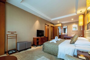Habitación de hotel con cama, televisión, escritorio con silla, armario y baño visible a través de una puerta abierta.