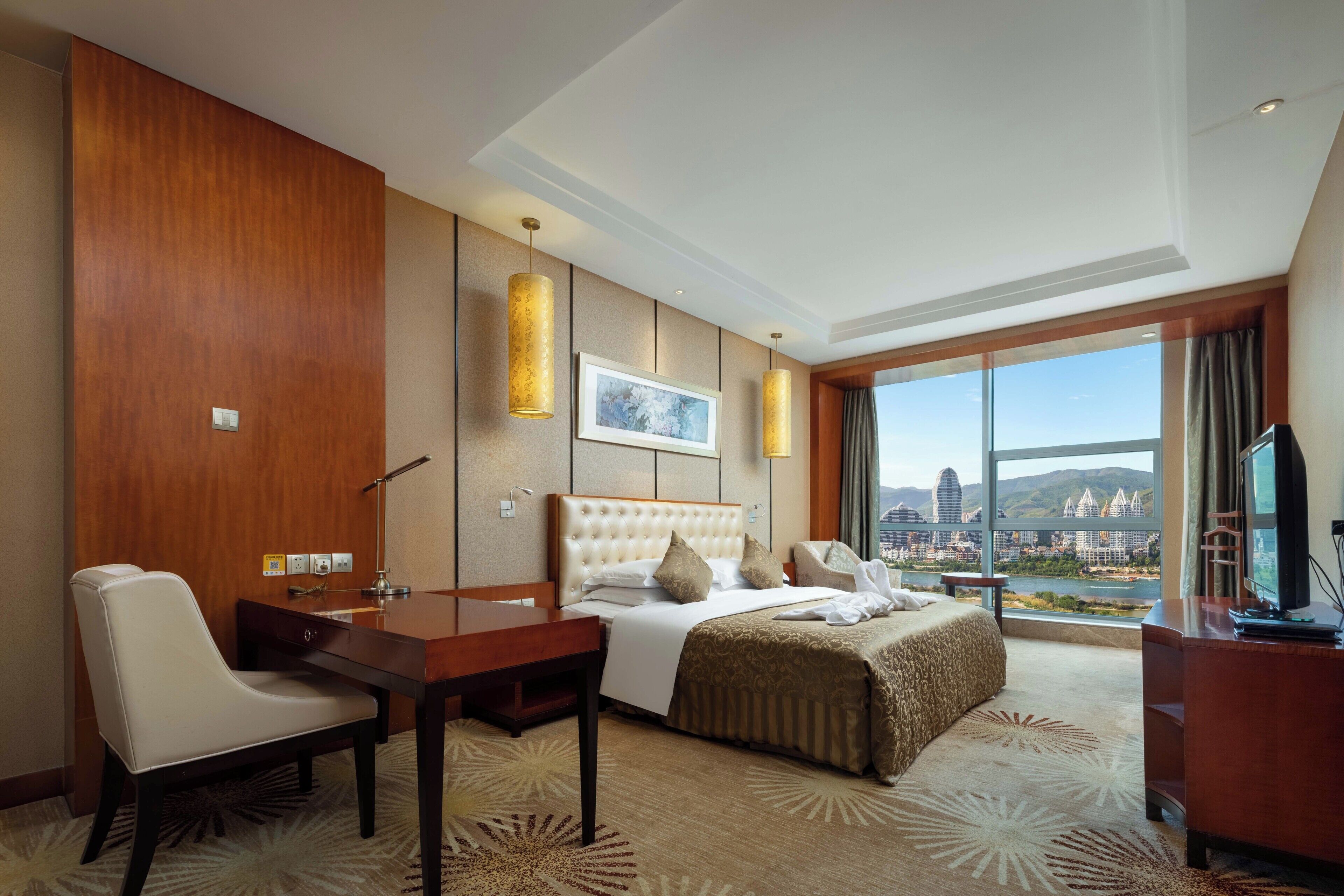A hotel room with a bed, a desk, a chair, a television, and a large window offering a city view.