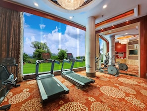 Un gimnasio de hotel con cintas de correr, equipo de ejercicio y un amplio ventanal con vistas a un paisaje verde.