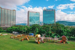 Un parque con equipo para juegos infantiles y un gran edificio de hotel al fondo.