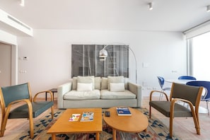 Ein modernes Wohnzimmer mit einer Couch, zwei Sesseln, einem Couchtisch und einem Essbereich mit Stühlen.