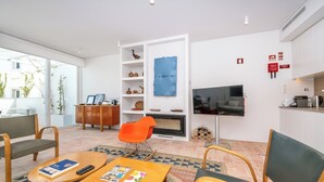 A modern living room with a fireplace, a television, and a dining area with a table and chairs. - Les Terrasses B / Private Rooftop Pool in Tavira (tavira)