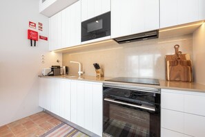 Une cuisine moderne avec des meubles blancs, un four encastré, un four à micro-ondes et une planche à découper en bois.