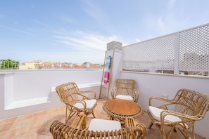 Eine Dachterrasse mit Korbmöbeln, einem kleinen runden Tisch und Blick auf die Stadt.