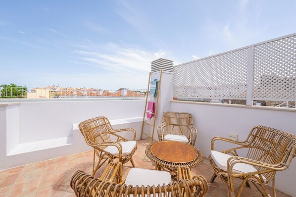 Una terraza en la azotea con mobiliario de mimbre, una mesita redonda y vistas a la ciudad.
