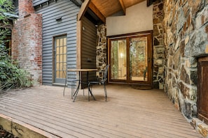 A wooden deck with a table and chairs, a stone wall, and a door leading to an interior space. - Olinda Birch by Ready Set Stay (Olinda)