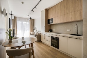 A modern kitchen with a dining area, wooden cabinets, a built-in microwave, and a dishwasher. - Kierbedzia Harmony Premium, Free Parking & WiFi (Warszawa)