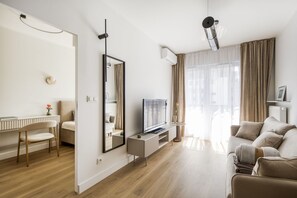 A modern living room with a flat-screen TV, a sofa, a dining area with a table and chairs, and a large window with curtains. - Kierbedzia Harmony Premium, Free Parking & WiFi (Warszawa)