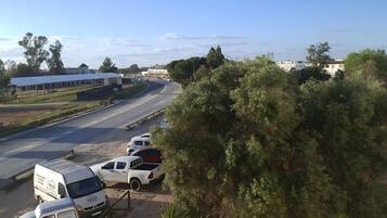 A road with parked vehicles, a clear sky, and greenery.