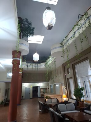 A spacious lobby with a high ceiling, hanging plants, and a reception desk.