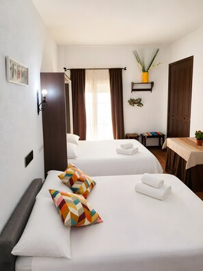 A hotel room with two beds, a small table, a potted plant, and a door.