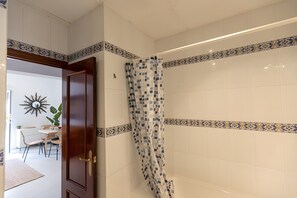 Een badkamer met witte tegels, een douchegordijn met een blauw-wit patroon, en een houten deur.