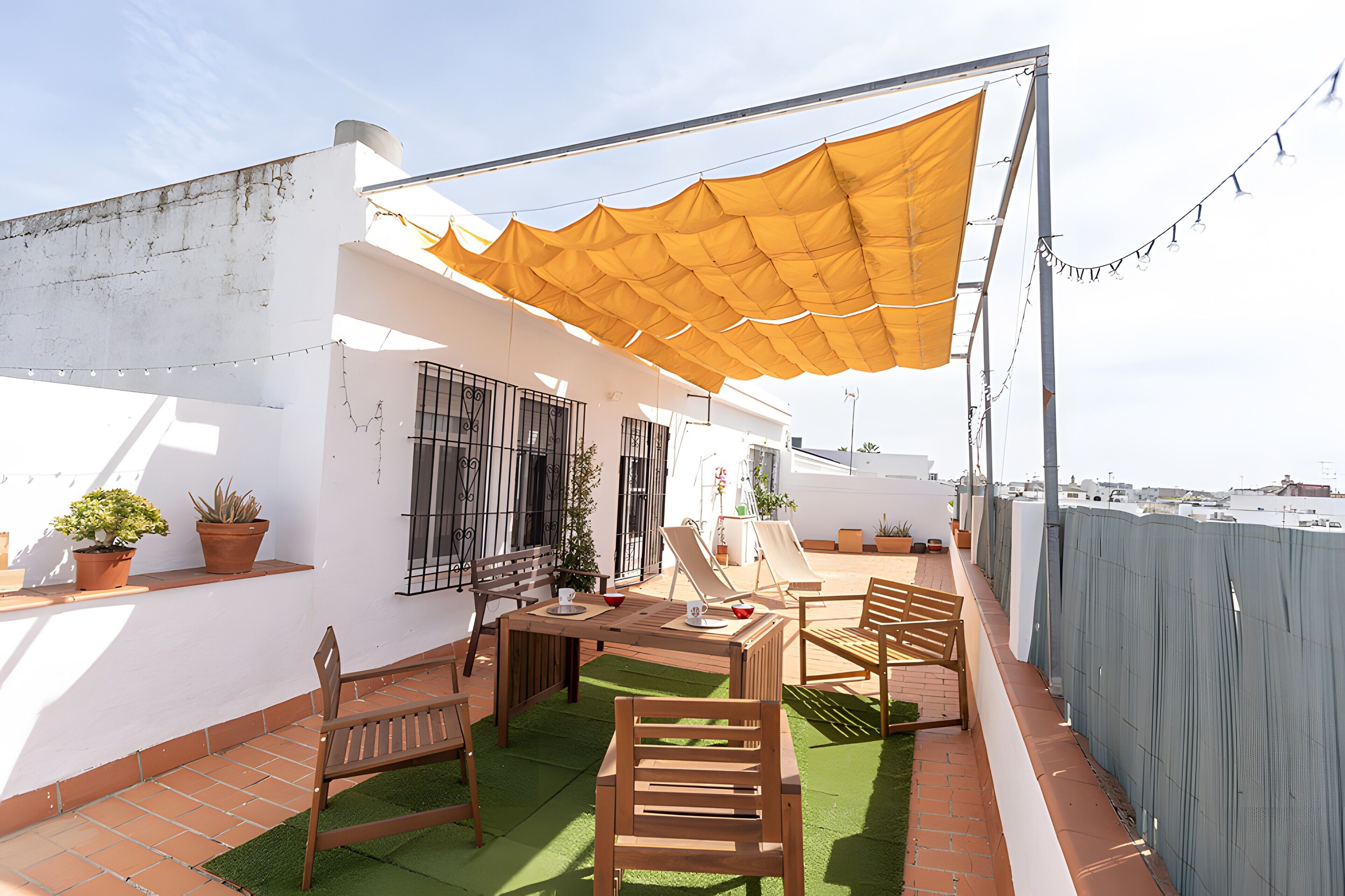 En udendørs terrasse med et bord, stole, plantekrukker og et gult markise.
