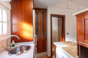 A compact kitchen with a stainless steel sink, wooden cabinets, and a door leading to a bathroom. - Ático Maravilla Sol – Bright Penthouse on 3rd Floor with Terrace (Seville)