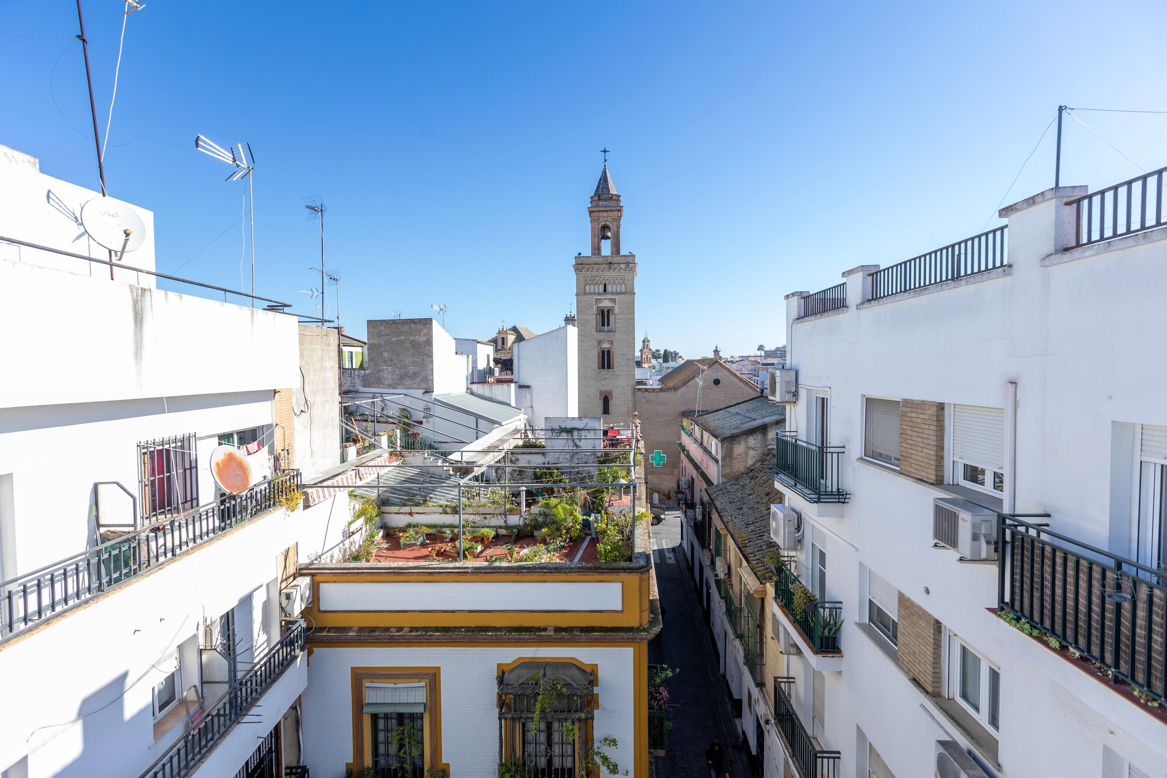 A narrow street with buildings on either side, a church with a bell tower, and a clear blue sky.
