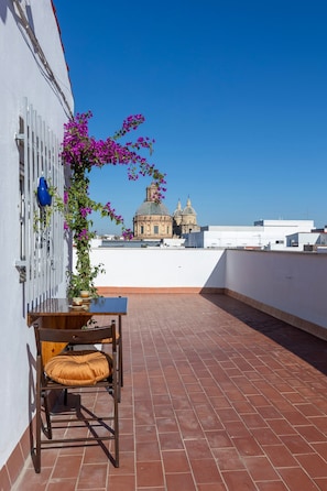 A rooftop terrace with a chair and table, a potted plant with purple flowers, and a building with domed architecture in the background. - Ático Maravilla Sol – Bright Penthouse on 3rd Floor with Terrace (Seville)