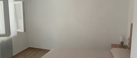 Un dormitorio con cama, lámpara colgante, ventana con cortinas y radiador.