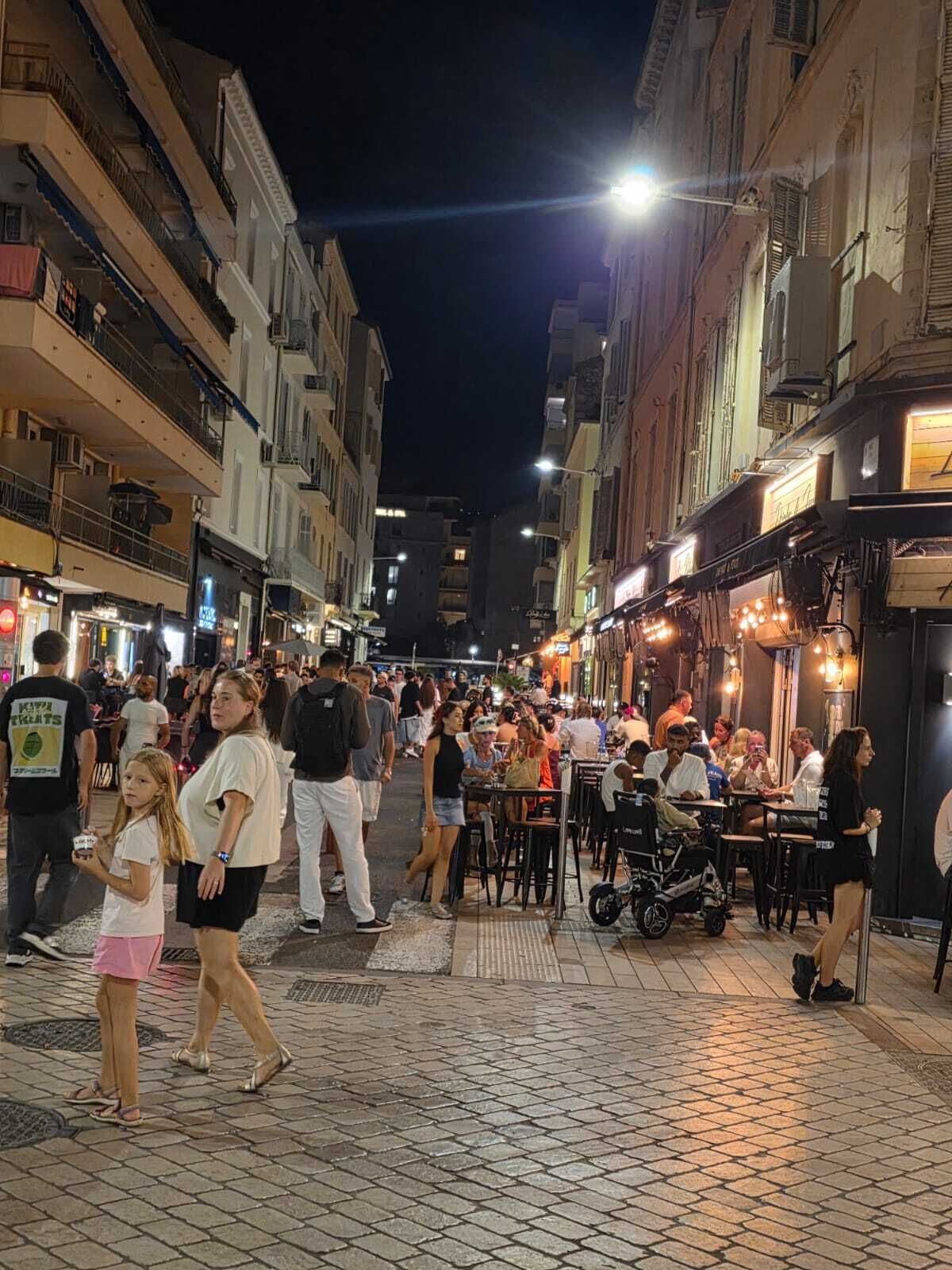 Escena de carrer animada a la nit amb gent caminant i dinovant a l'aire lliure.
