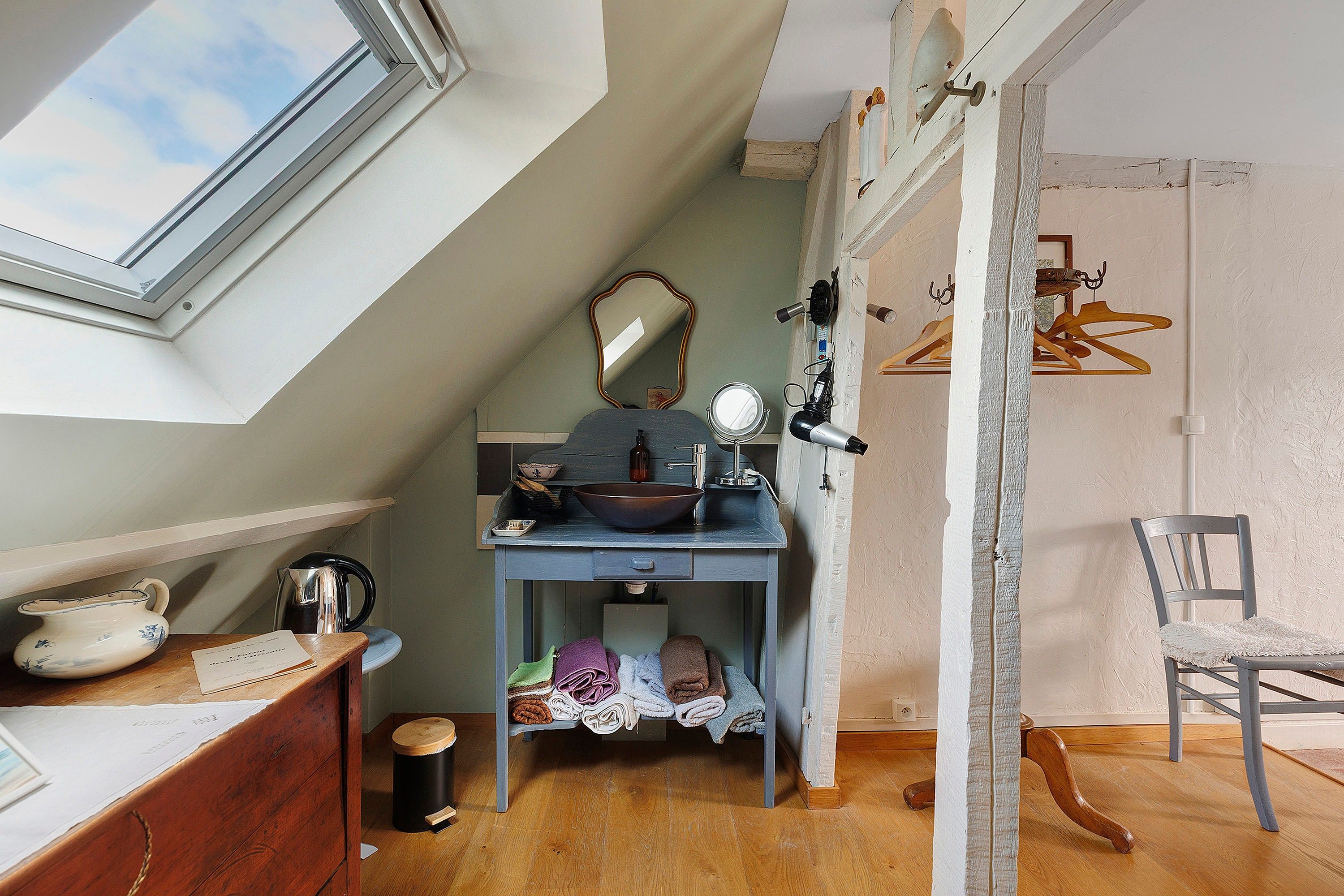 A compact, well-lit room with a skylight, a small sink, a mirror, and a chair.