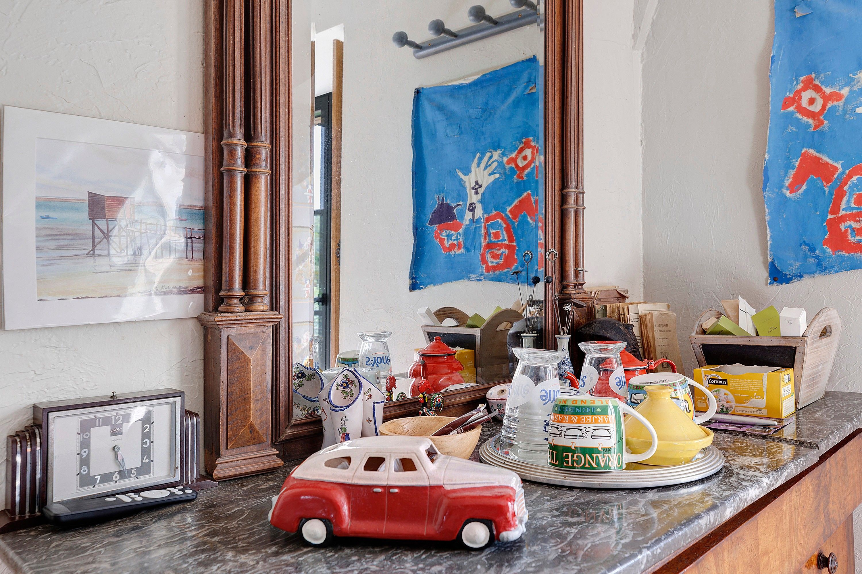 A cluttered room with a vintage car model, a clock, and various items on a counter.