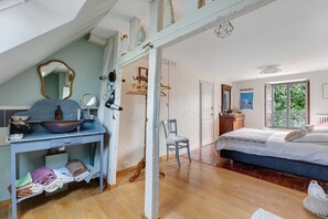 A bedroom with a large bed, a dresser, a mirror, and a window with a view of greenery.