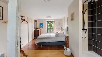Een slaapkamer met een bed, nachtkastje, hanglamp, raam en een badkamer met douche.
