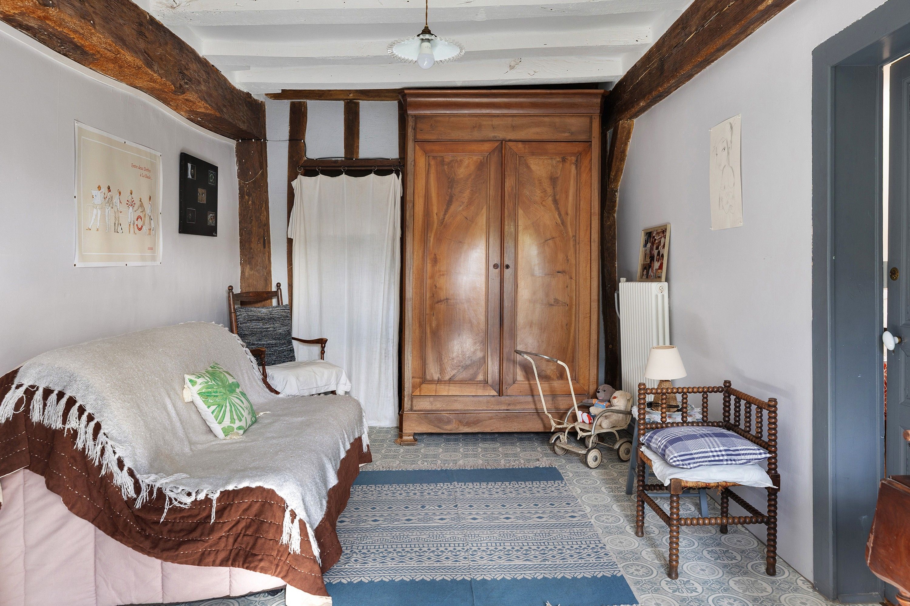 A room with a bed, a chair, a wooden wardrobe, a radiator, and a wall with pictures.