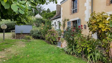Un jardin résidentiel avec une pelouse, diverses plantes et une maison en briques dotée de volets.