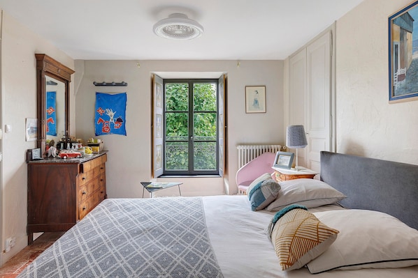 A bedroom with a bed, dresser, window, and artwork on the walls.