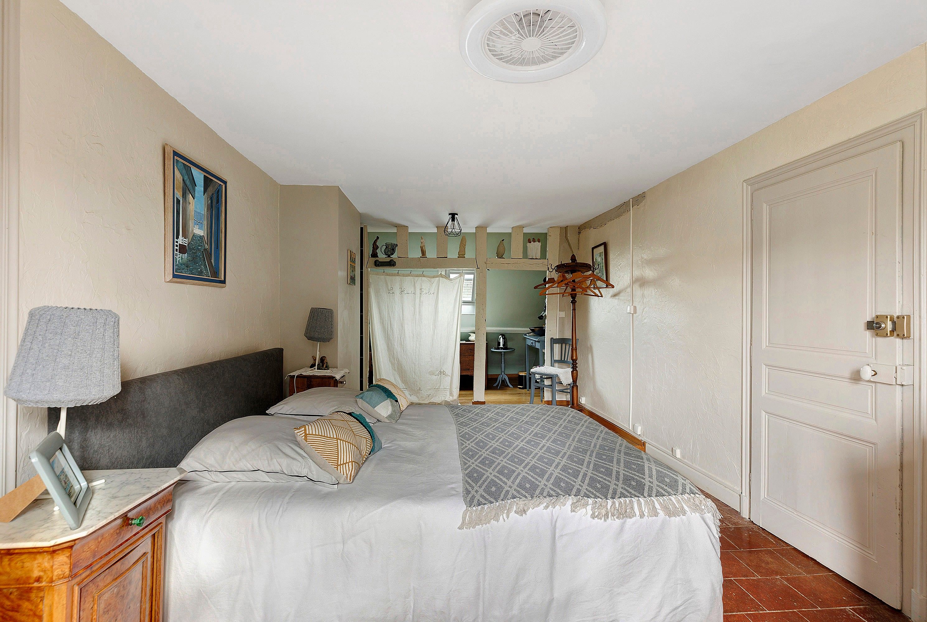 Une chambre à coucher avec un lit, des tables de chevet, une lampe, un tableau et une porte.