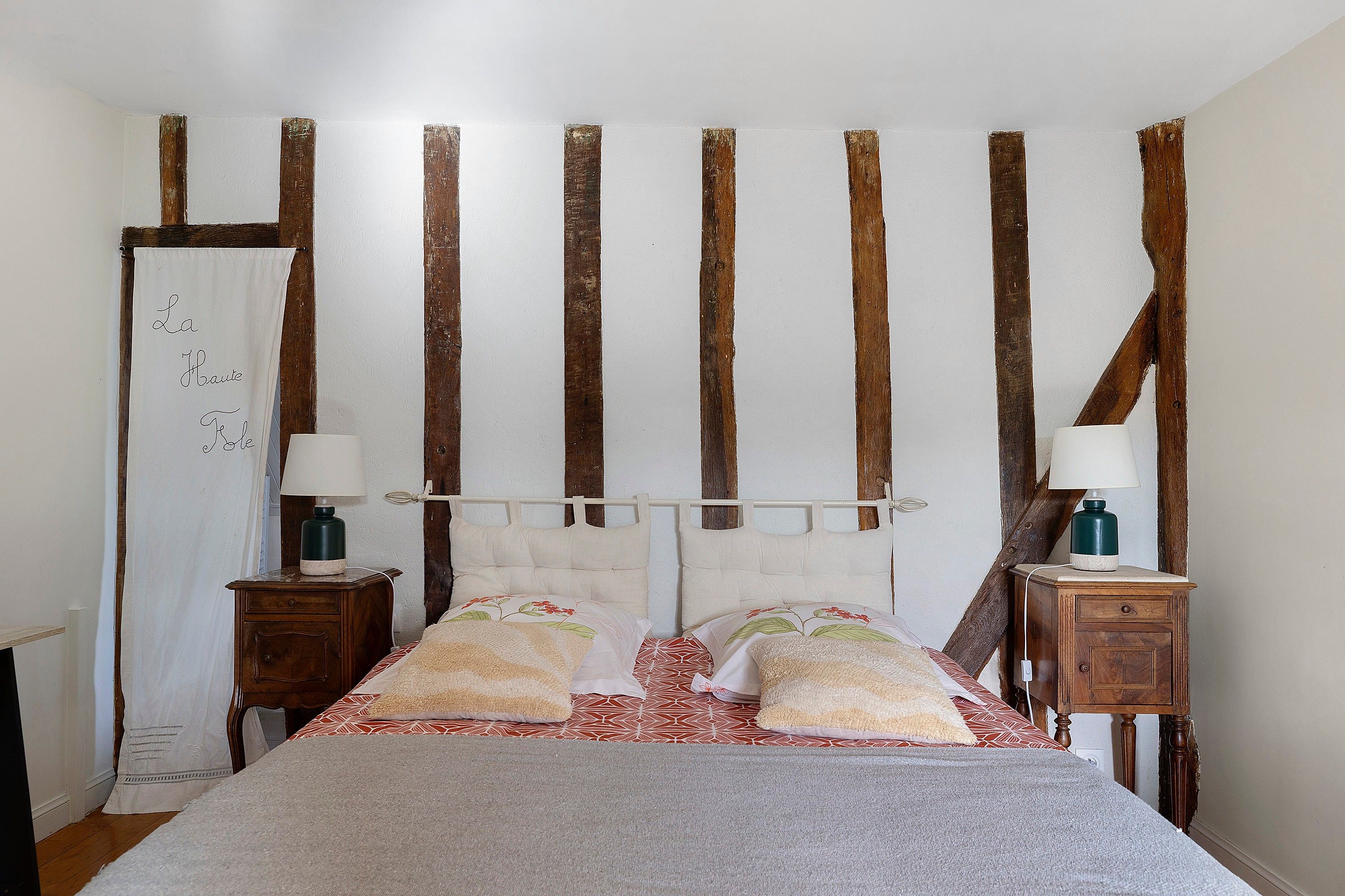 Une chambre à coucher comprenant un lit, deux tables de chevet, une petite table, une tête de lit en bois et un tableau blanc.