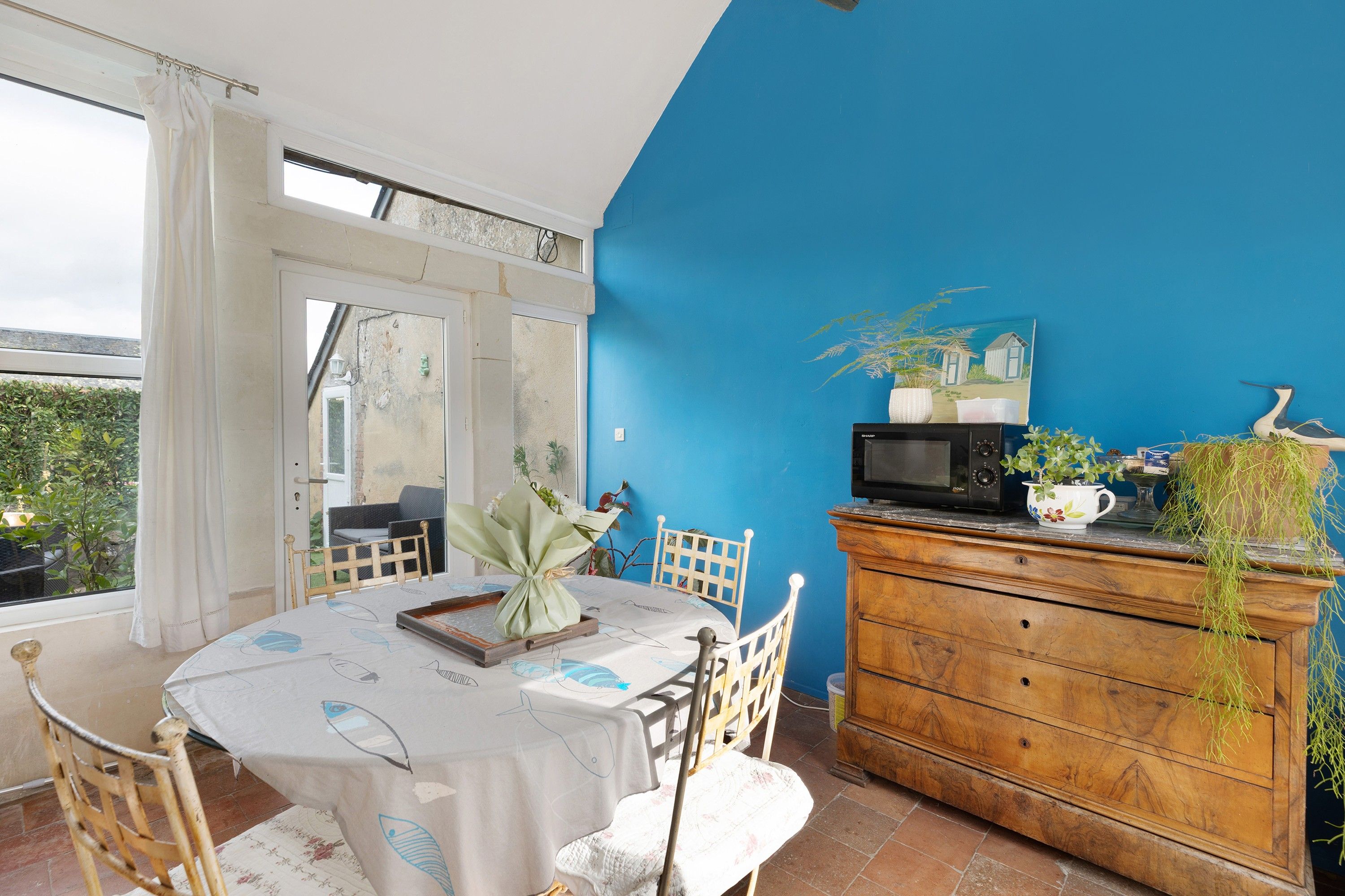 Un coin repas avec une table dressée pour deux personnes, un meuble en bois contenant un four à micro-ondes et une vue sur l’extérieur.