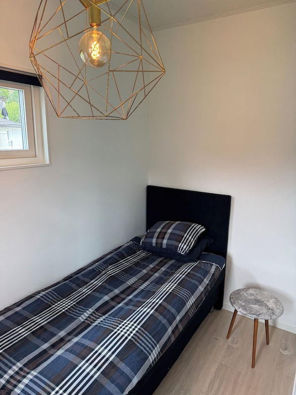A single bed with a plaid bedspread, a black headboard, and a geometric pendant light fixture.