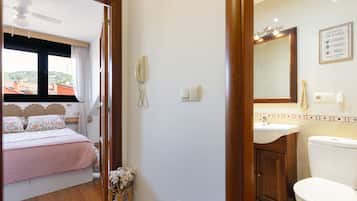 A hotel room with a bed, a bedside telephone, a bathroom with a sink, mirror, and toilet.
