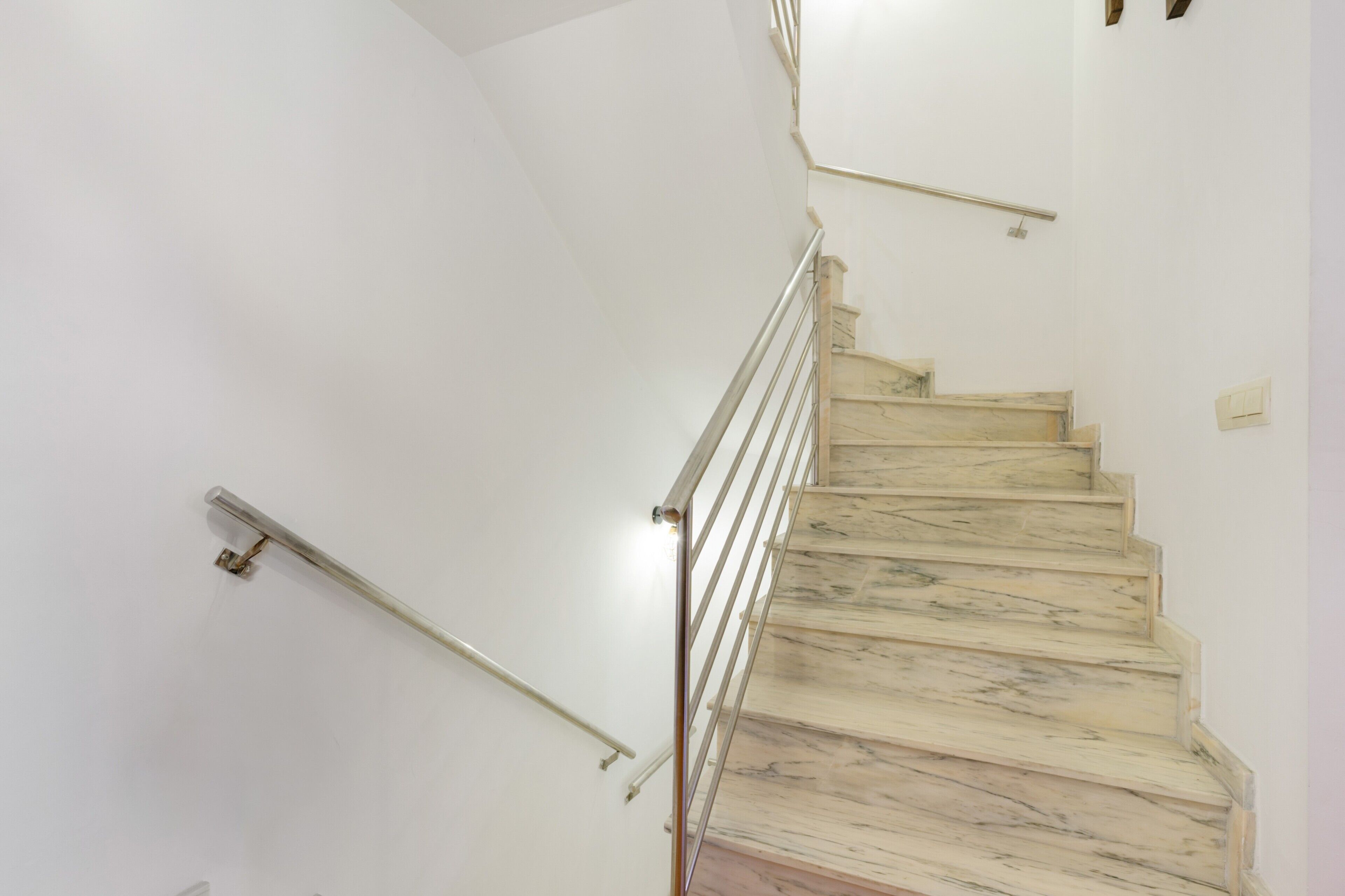 A marble staircase with metal handrails and a light fixture on the wall.