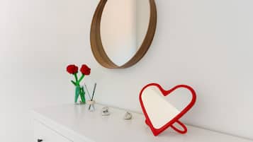 A white dresser with a mirror, a heart-shaped light, and a vase with red flowers.