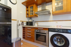 A kitchen with a washing machine, oven, microwave, and wooden cabinets.
