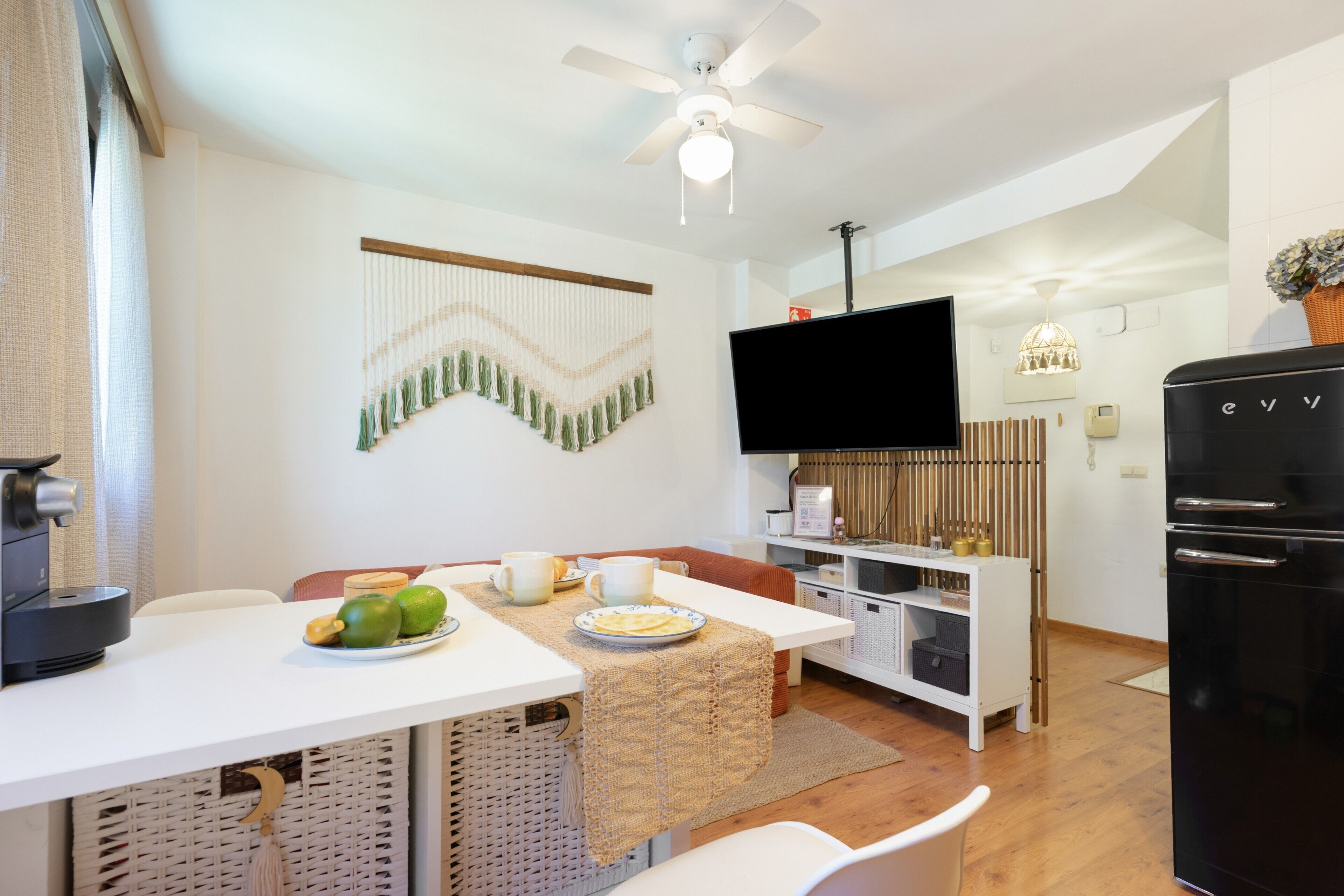 Una cocina moderna con comedor, televisor de pantalla plana montado en la pared y refrigerador negro.