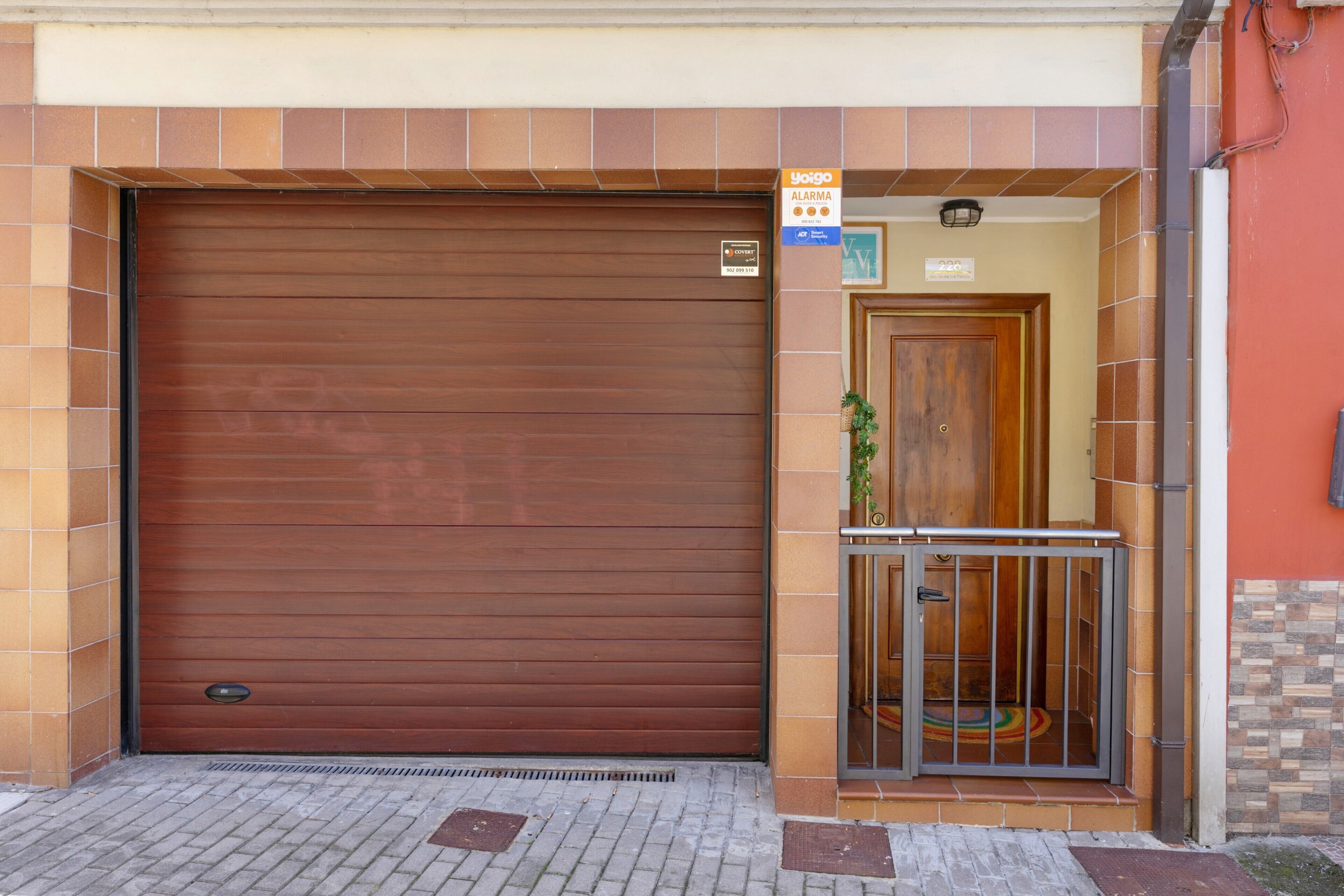 Puerta de garaje marrón cerrada con una reja metálica y un pequeño balcón con una planta.