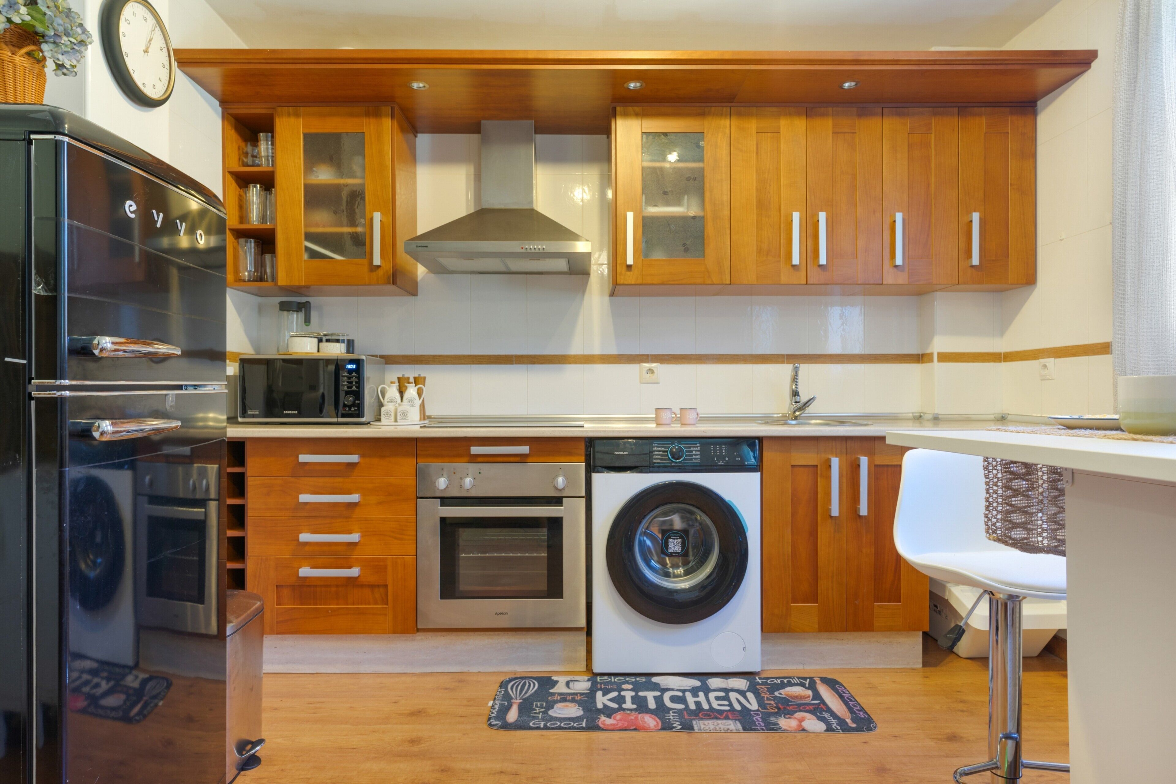Een kleine keuken met houten kastjes, een magnetron, een oven, een vaatwasser en een spoelbak.